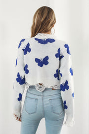 White acrylic cropped sweater with blue butterfly intarsia and frayed hem.