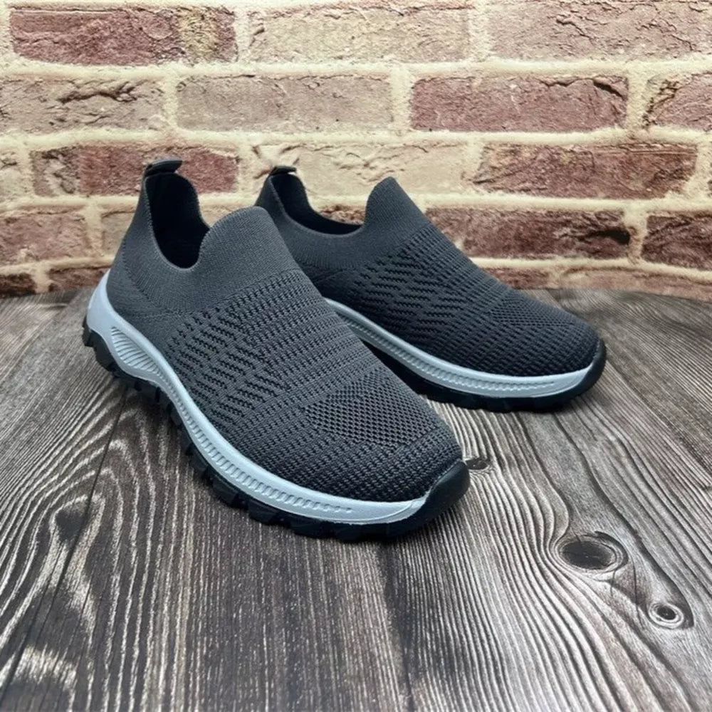 Grey breathable slip-on sneakers with round toe and textured knit upper.