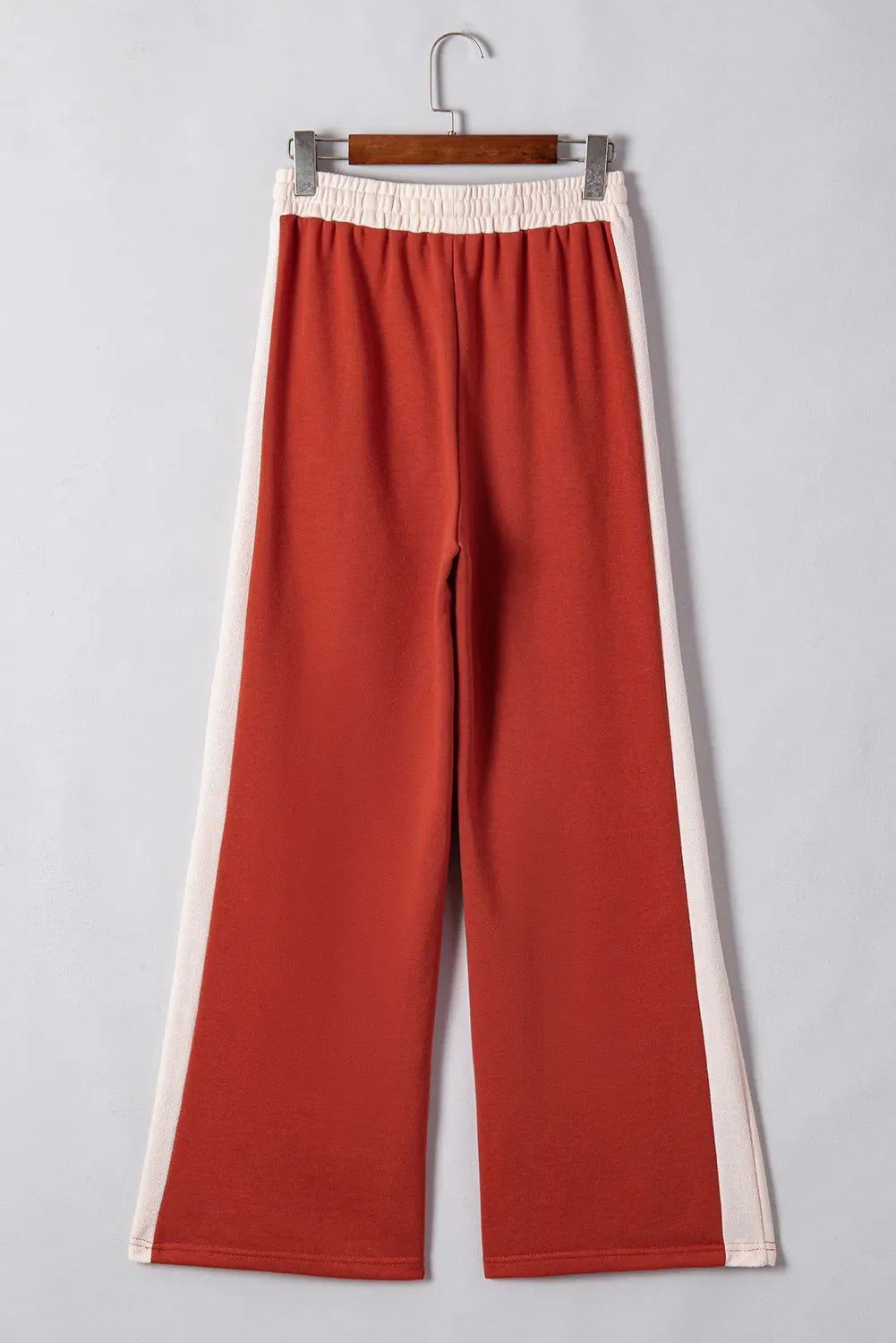 Terracotta-red track pants with cream side stripes and elastic waistband.