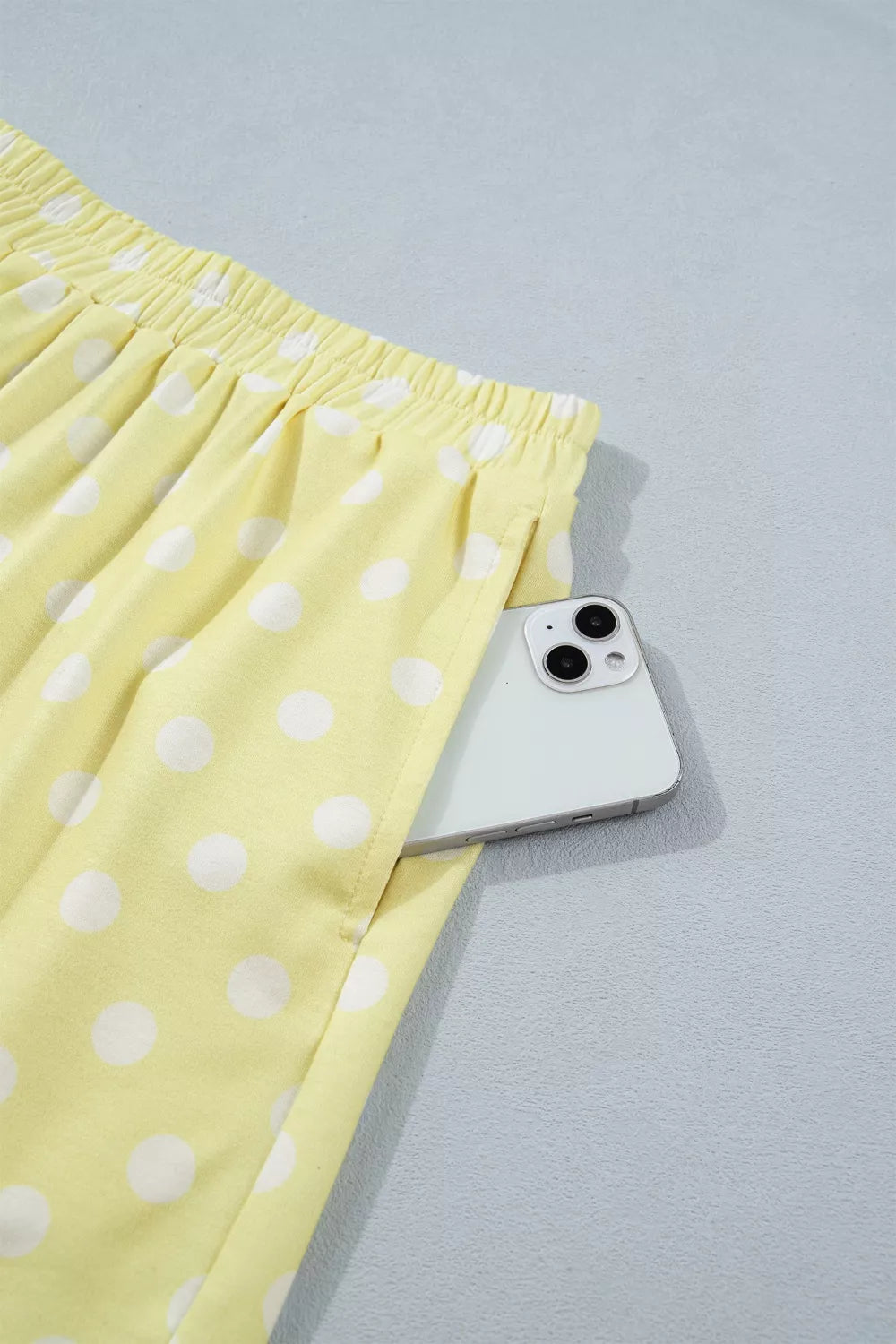 Pastel yellow polka dot shorts with elastic waist and side pocket holding a phone.