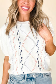 White cable knit sweater with puff sleeves and diamond pattern accents in pink, blue, and gray.
