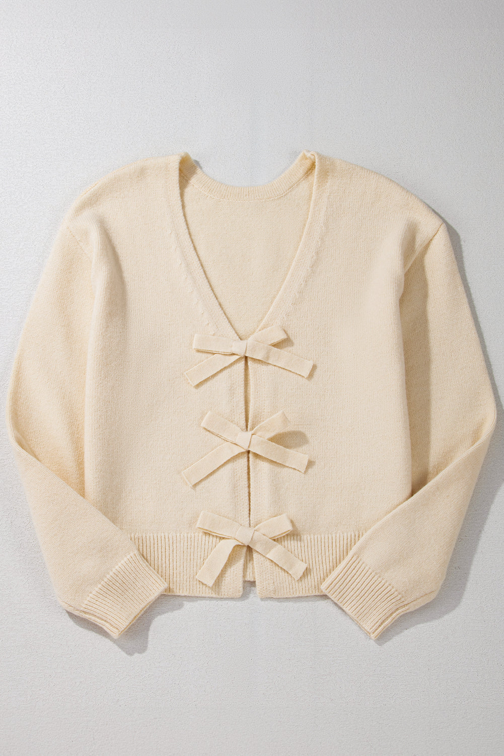 Ivory bouclé knit cardigan with v-neck and three front bow details.