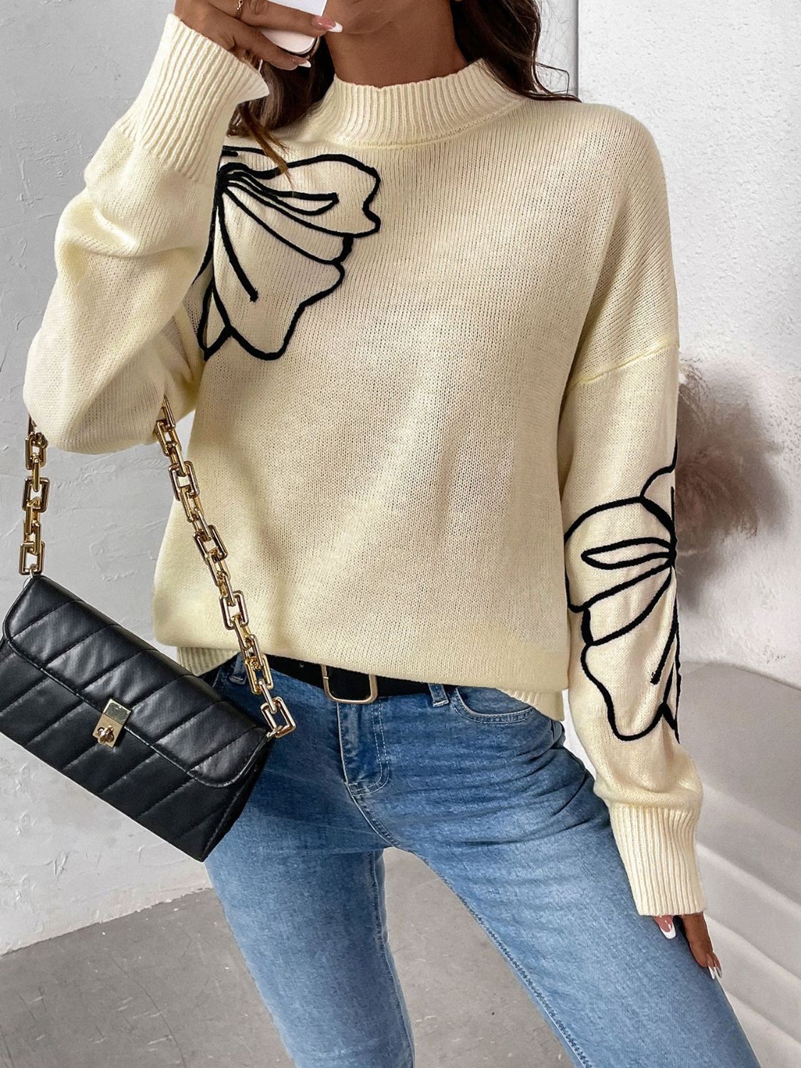 Pastel yellow acrylic knit sweater with black embroidered floral motifs on the chest and sleeves.