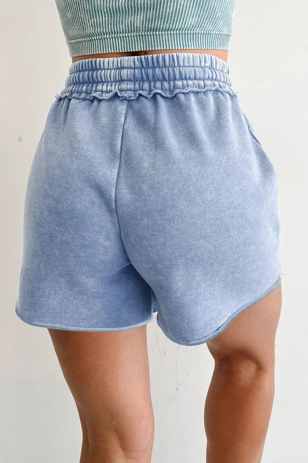Light blue acid-washed cotton drawstring shorts with pockets and ruffled elastic waistband.