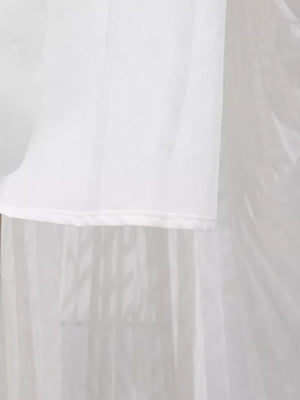 White maxi dress hem detail with sheer overlay and subtle vertical pleating.