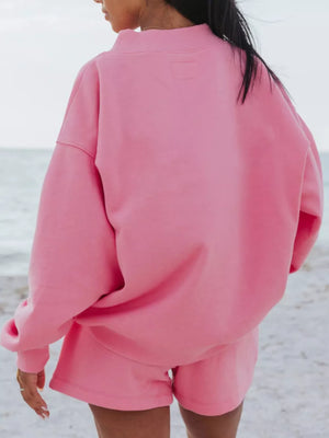 Pink crew neck sweatshirt and shorts lounge set on a beach.
