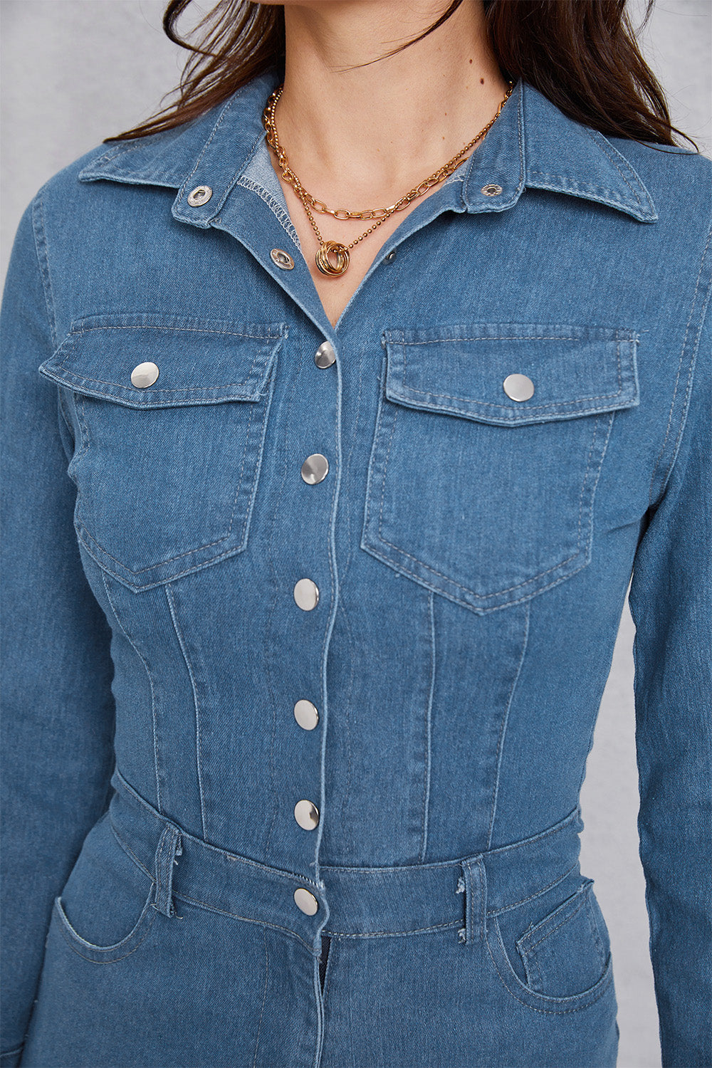 Medium wash denim utility jumpsuit with defined waist, button front, and chest pockets.