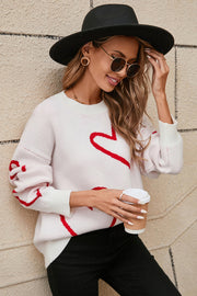White acrylic knit jumper with red heart outline pattern, crew neck, and long sleeves.