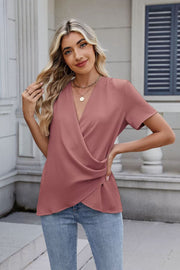 Dusty pink short sleeve blouse with draped crossover neckline and textured fabric.