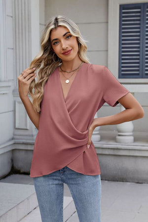 Dusty pink short sleeve blouse with draped crossover neckline and textured fabric.