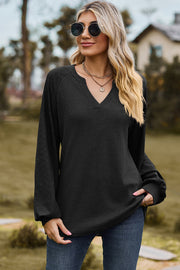 Black waffle knit raglan v-neck top with textured sleeves and a relaxed fit.
