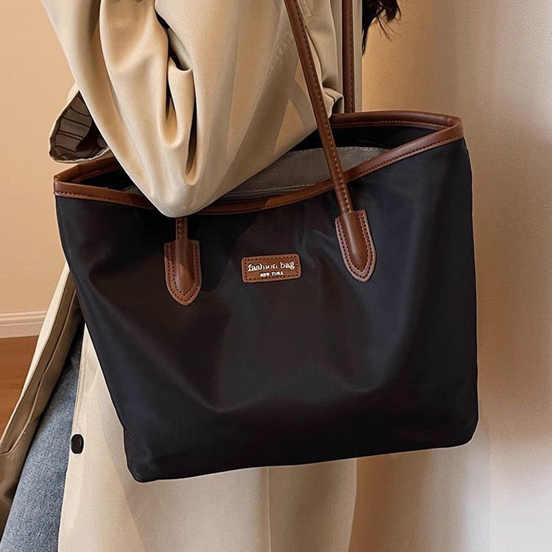 Black Oxford cloth tote bag with brown trim and handles, featuring a small logo patch.