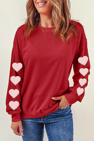 Deep red sweatshirt with pink heart appliqué details on the sleeves.