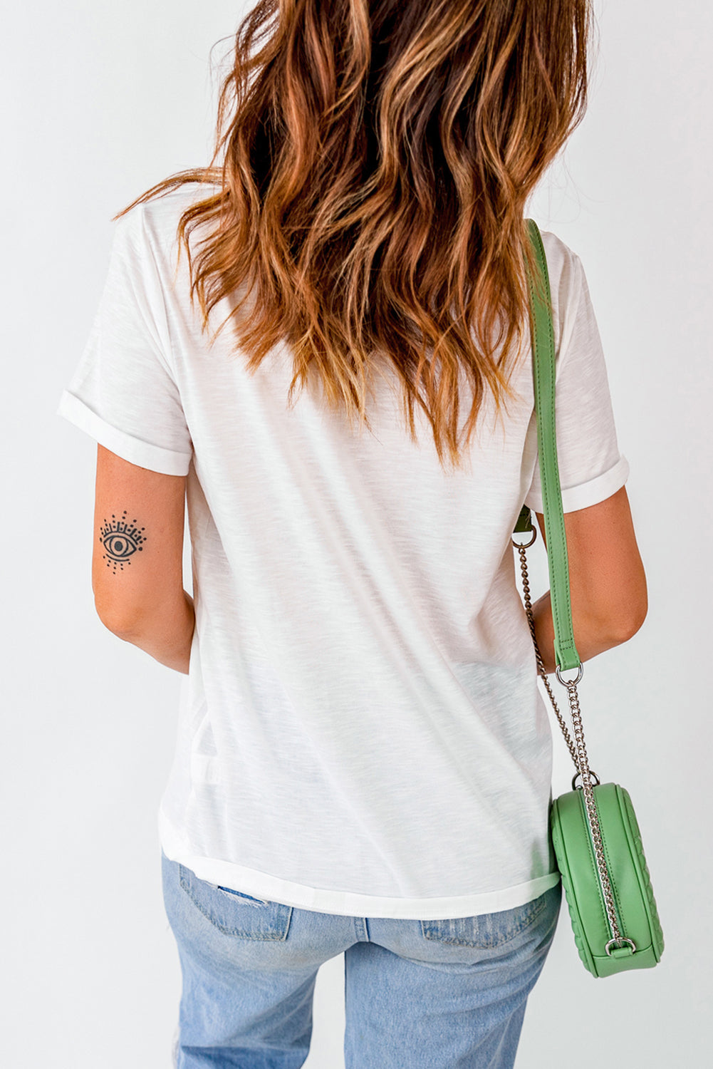White graphic t-shirt with rolled sleeves and a subtle eye tattoo on the arm.