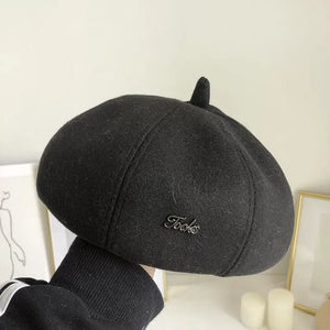 Black woolen beret with paneled design and decorative pin detail.
