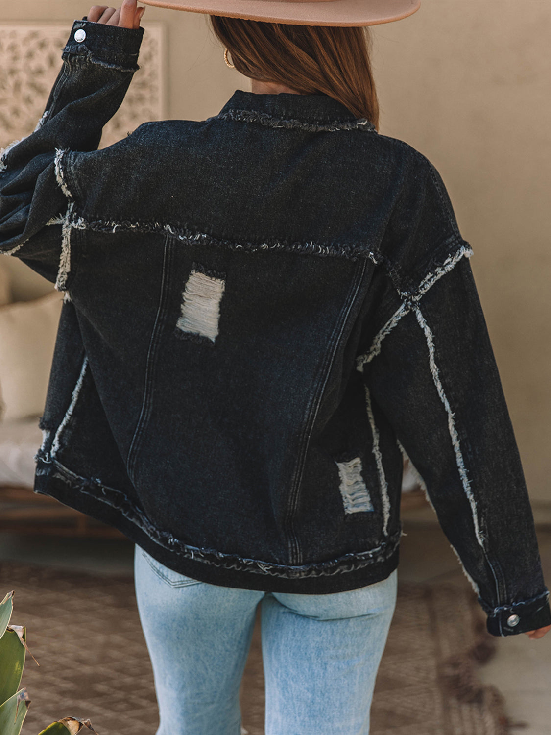 Black denim trucker jacket with raw hem, distressed details, and button closure.