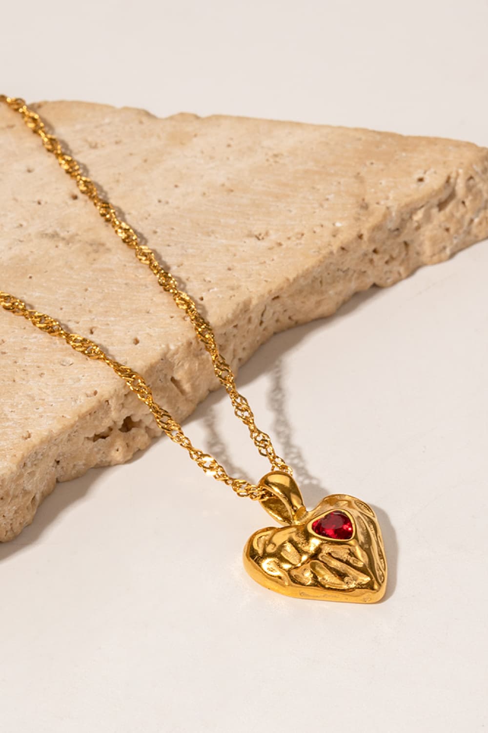 Gold textured heart pendant necklace with red gemstone on a delicate chain.