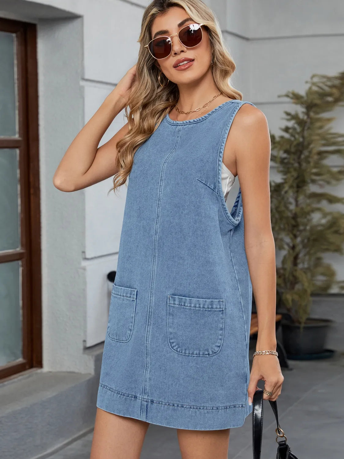 Sleeveless light blue denim pinafore dress with front pockets and a rounded neckline.