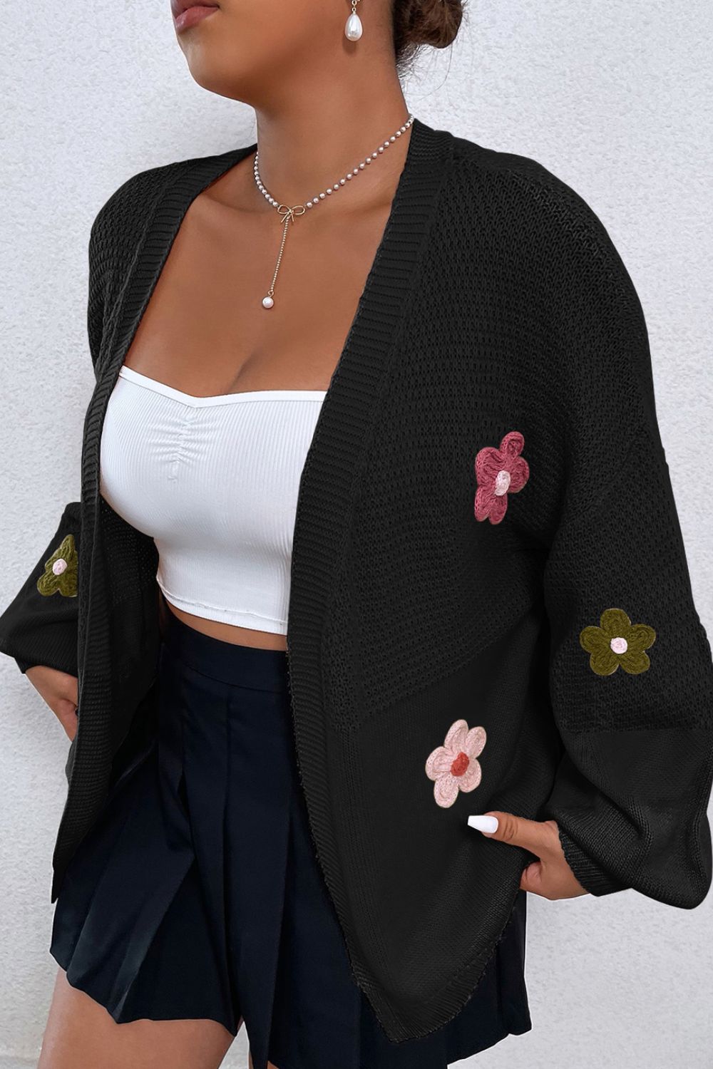 Black knit cardigan with embroidered floral appliques on sleeves and front.