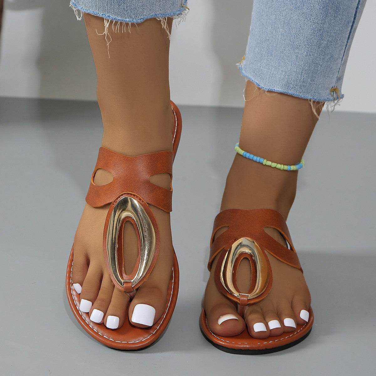 Brown open-toe sandals with golden oval accent and cut-out details.