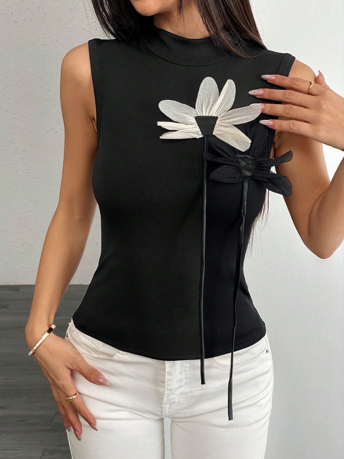 Black ribbed mock neck sleeveless top with floral appliqué detail and ties.