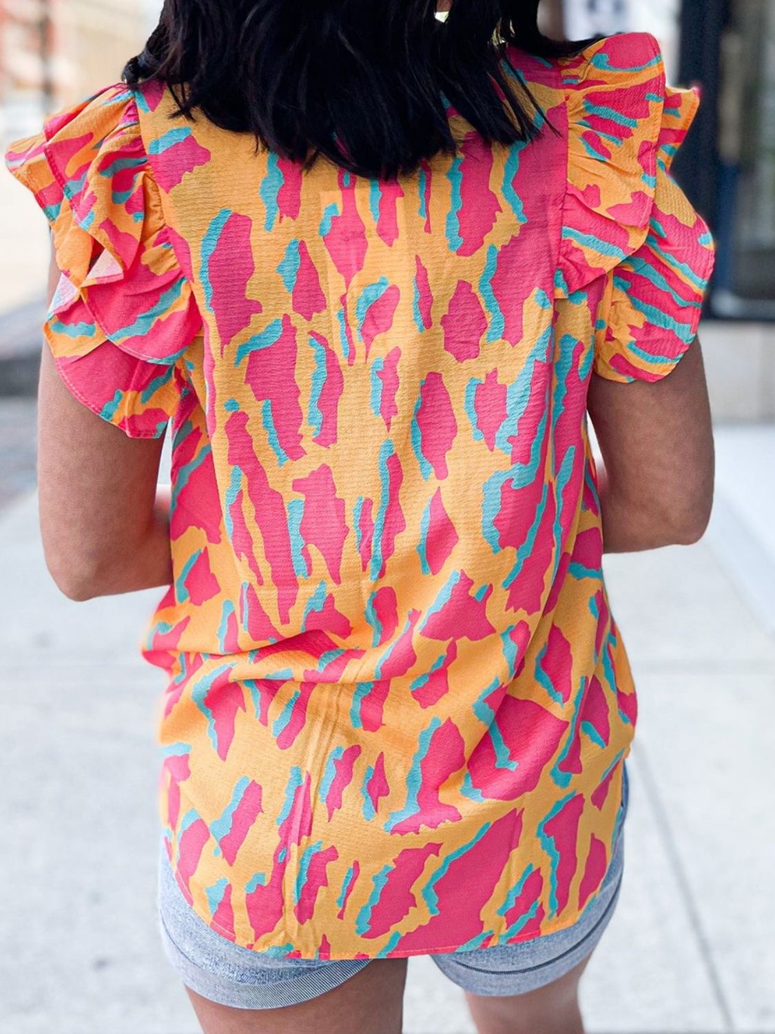 Neon abstract ruffle sleeve blouse in multicolor with pink and teal animal print on orange.