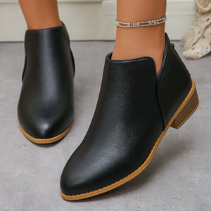 Black V-cut pointed toe block heel boots with a low heel and tan sole.