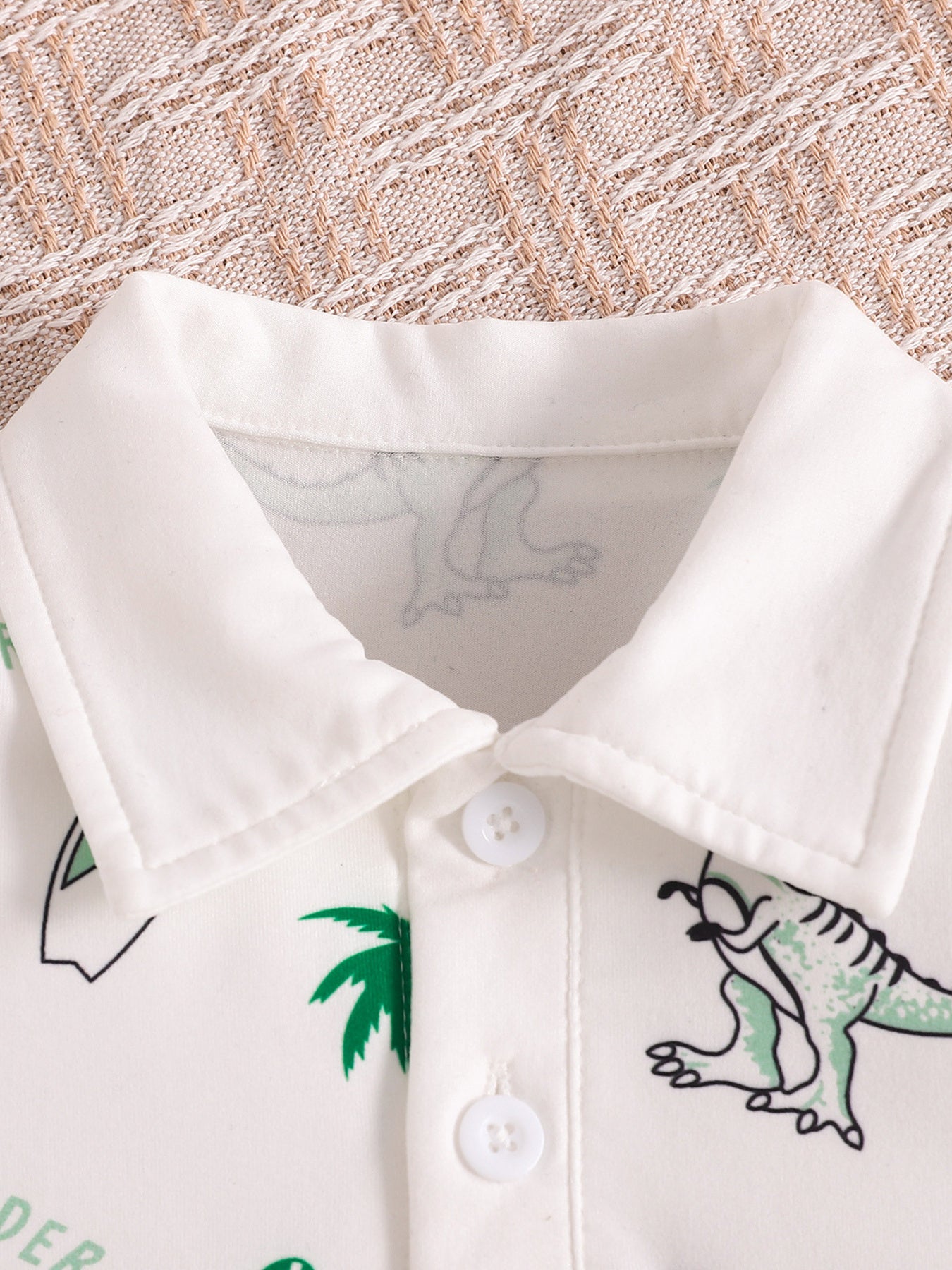 White baby polo shirt with dinosaur print and green palm trees, featuring a collar and button placket.