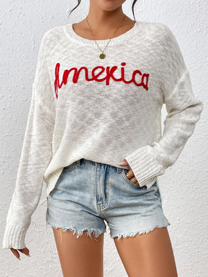 Ivory knit sweater with red embroidered "America" text, crew neck, long sleeves.