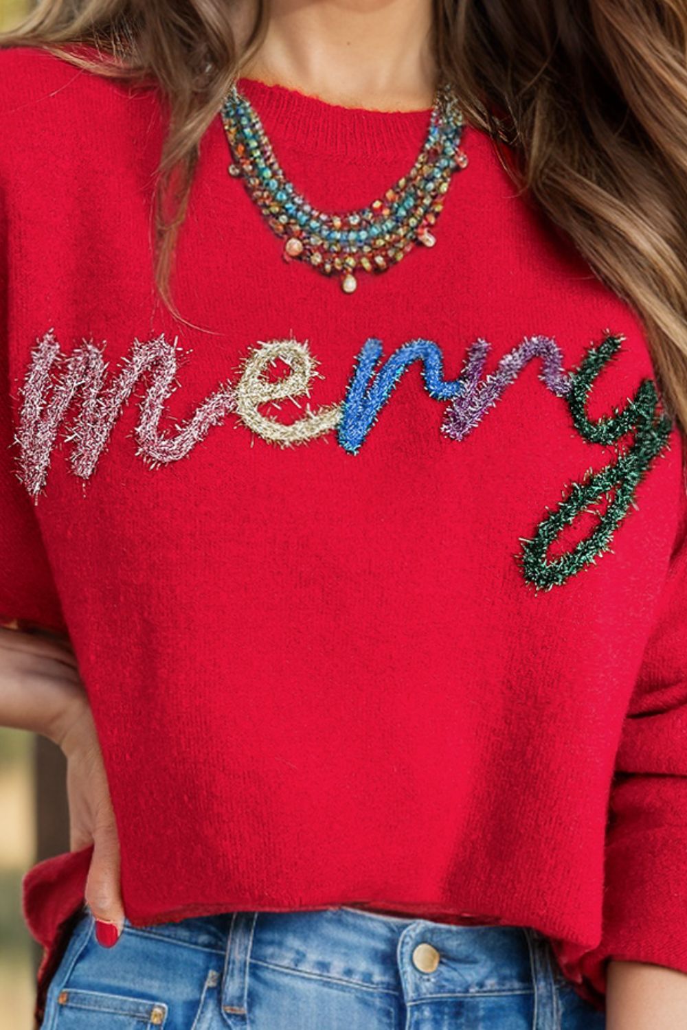Red knit crewneck sweater with embellished "Merry" text detail.