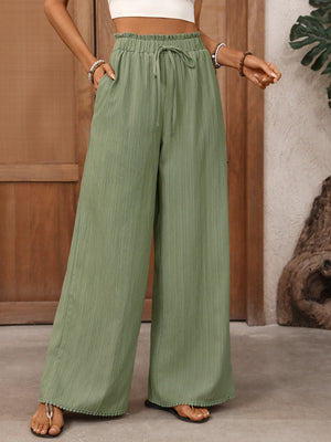 Crinkled wide-leg maternity pants in green with drawstring waist and pom-pom hem detail.