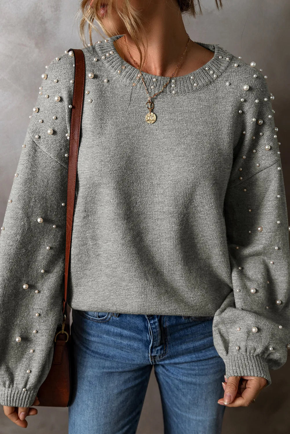 Gray pearl-embellished long sleeve sweater with crew neck, styled with jeans.