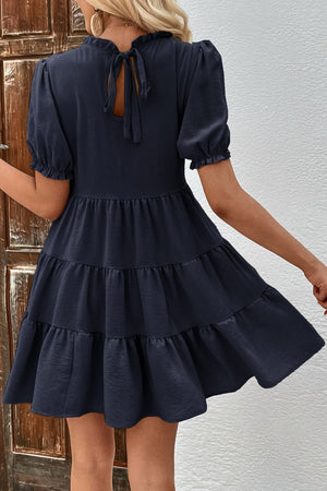 Dark blue tiered mini dress with ruffled neckline, puff sleeves, and back tie detail.
