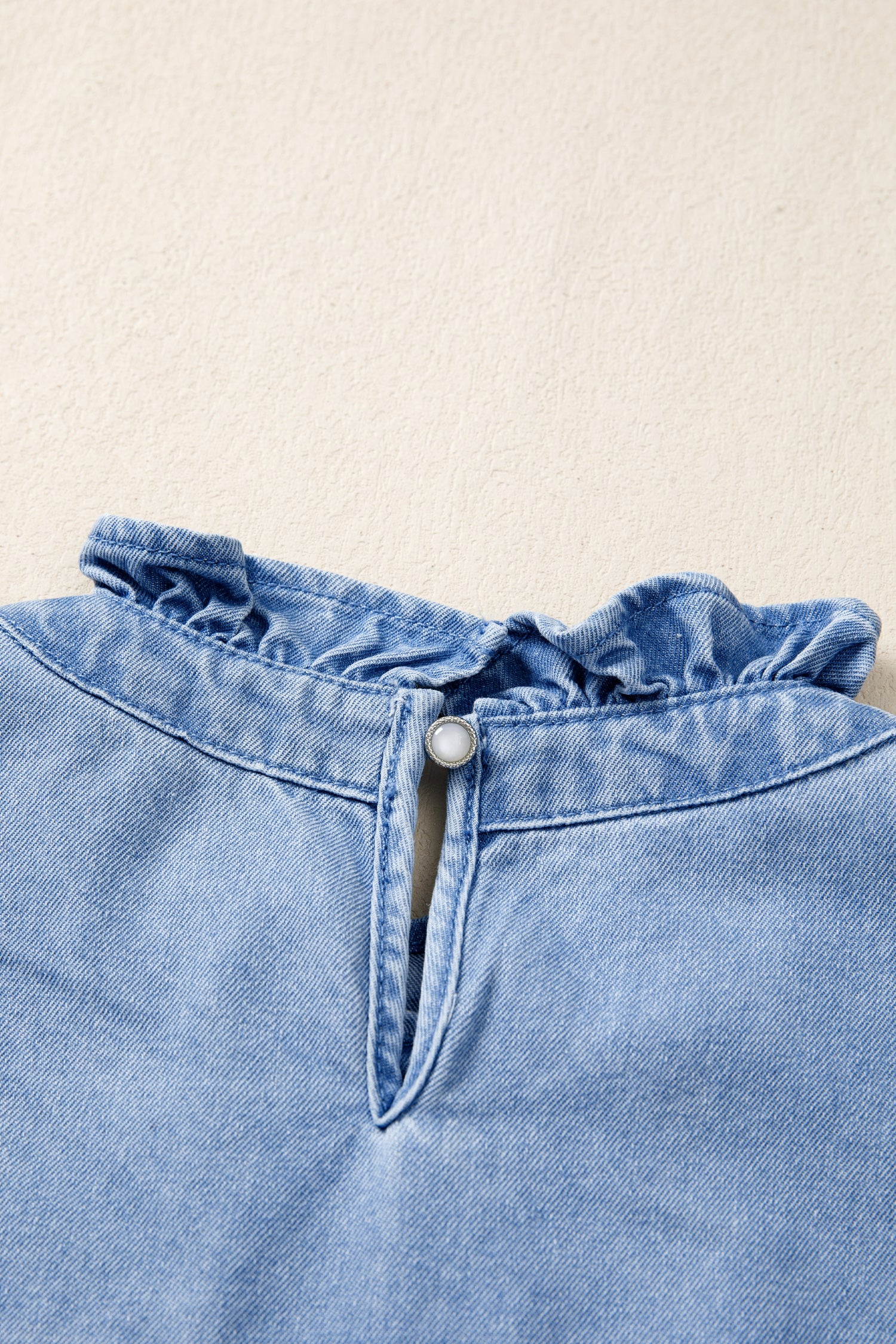 Light wash denim blouse with frilled collar and button keyhole detail.
