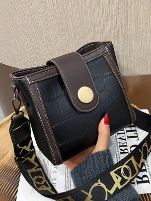 Black crocodile pattern mini crossbody bag with brown trim and gold button closure.