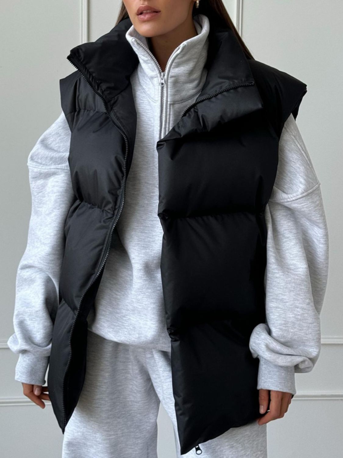 Black padded puffer vest with a high collar and zip front, worn over a grey sweatshirt.