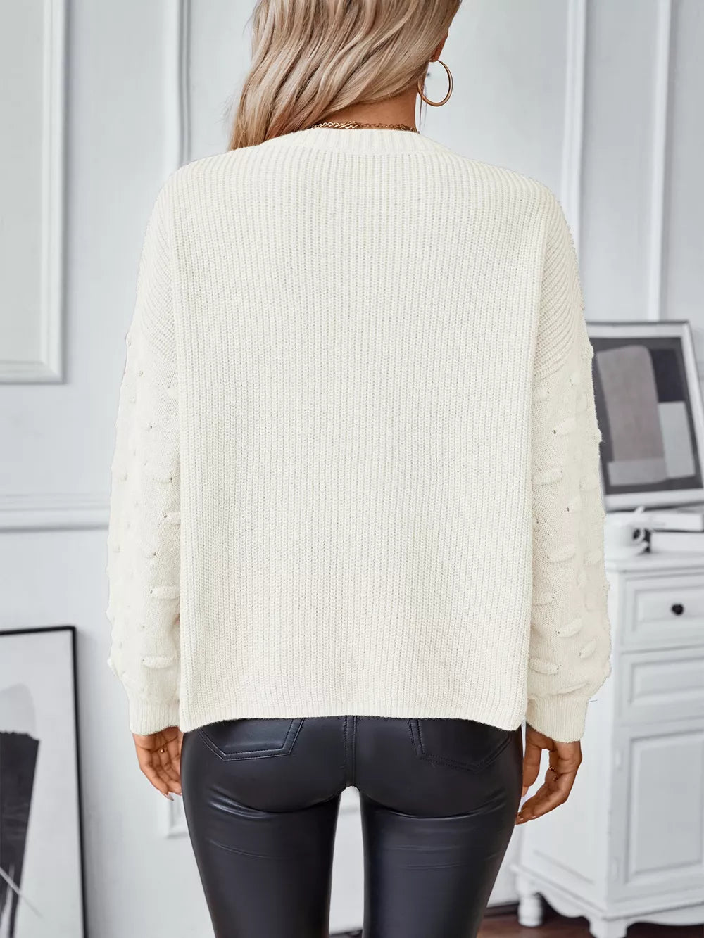 Chic ivory knit sweater with textured sleeve details and pockets, styled with black pants.