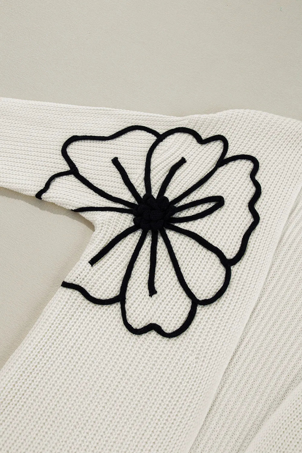 Ivory acrylic knit cardigan with black floral appliqué detail on sleeve