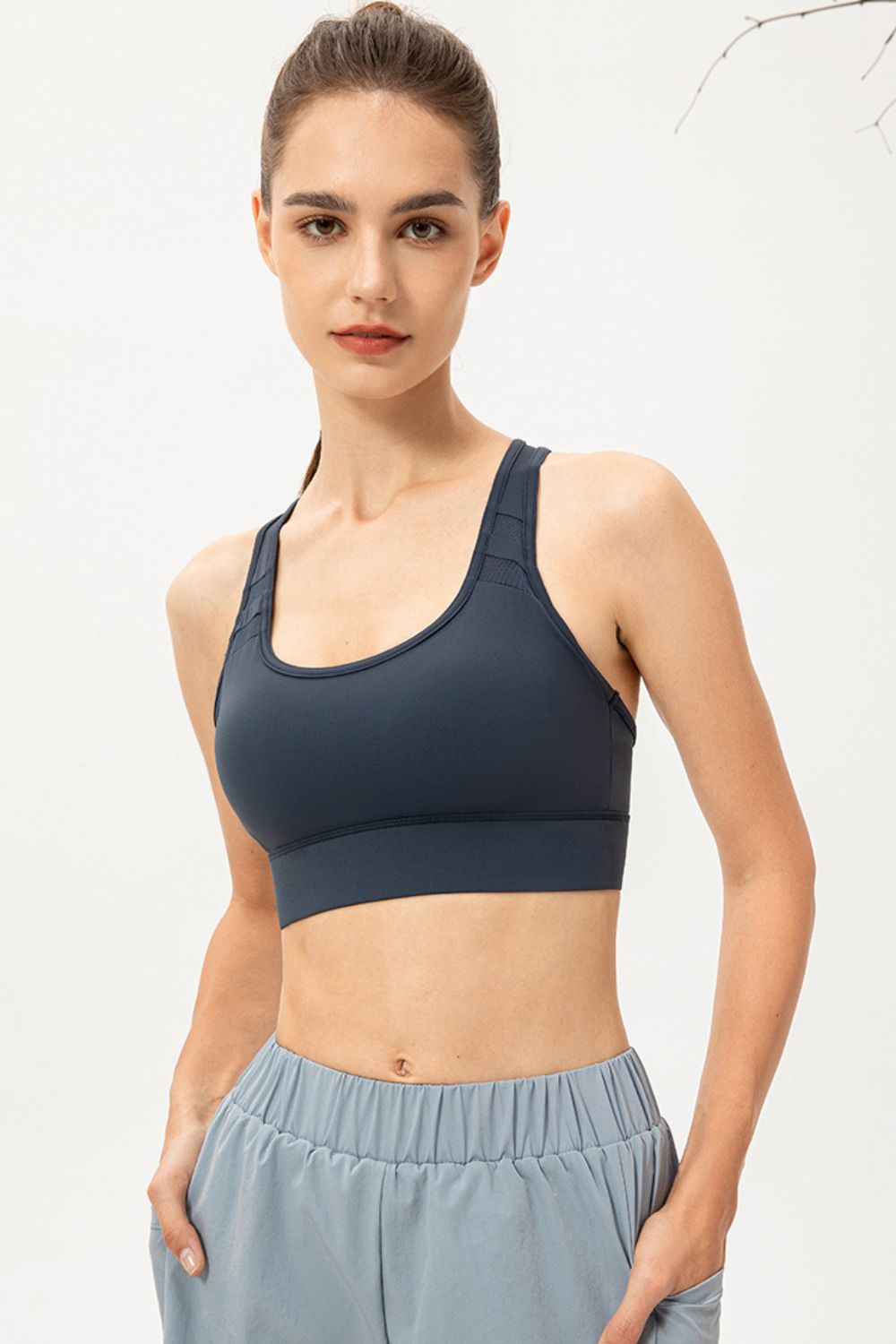 Mesh-inset performance sports bra in deep teal with scoop neck and racerback straps.