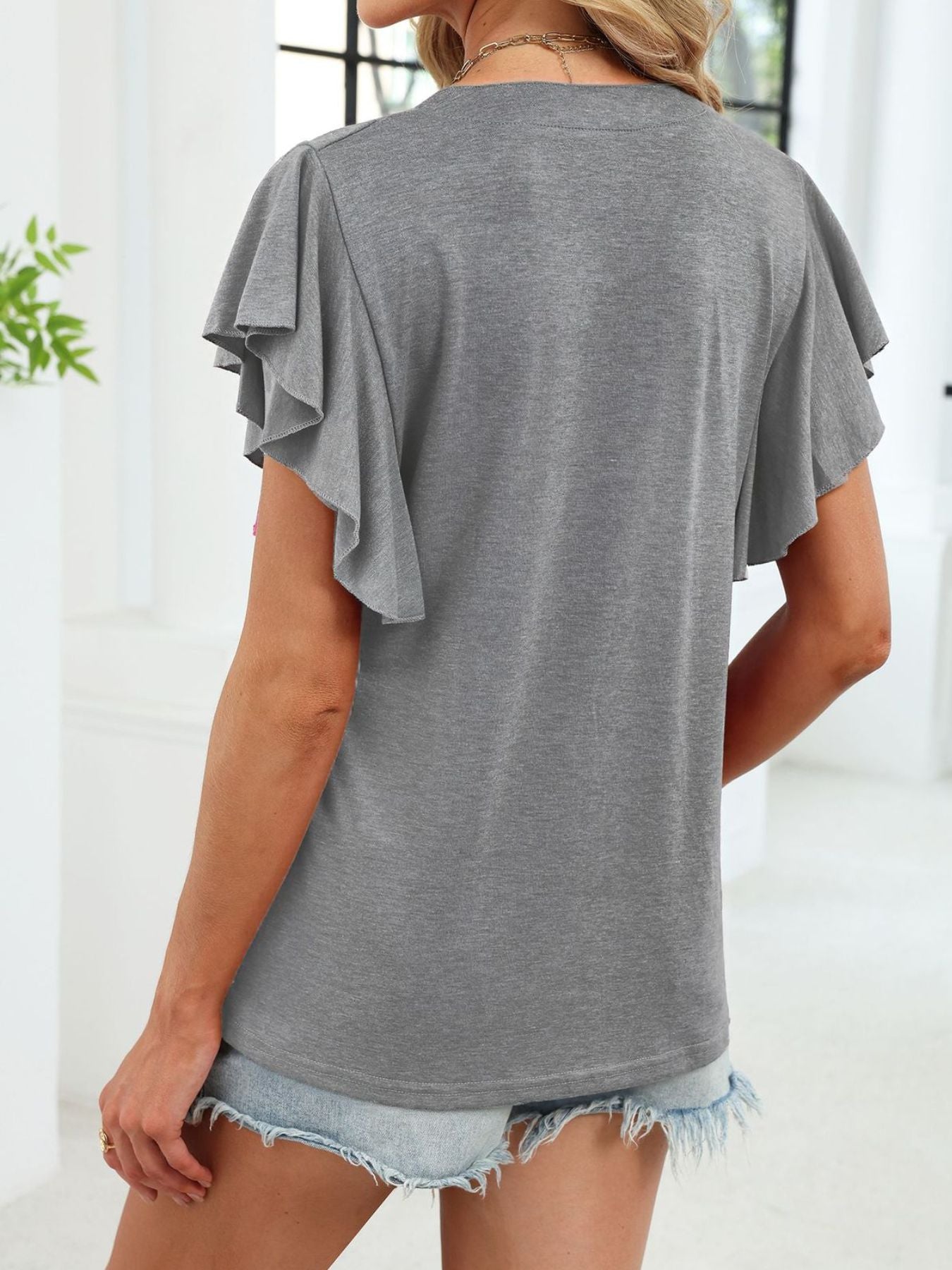 Gray t-shirt with ruffled short sleeves and a notched V-neck, paired with denim shorts.