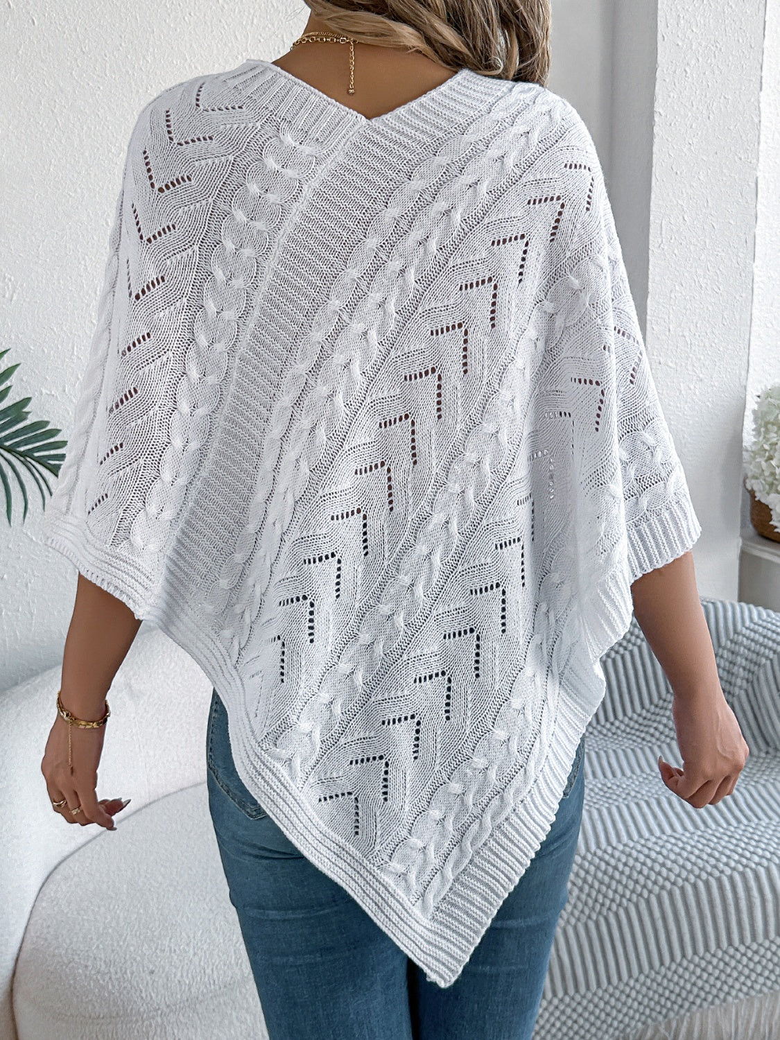 White cable knit poncho with chevron detail and V-neck, styled with jeans.