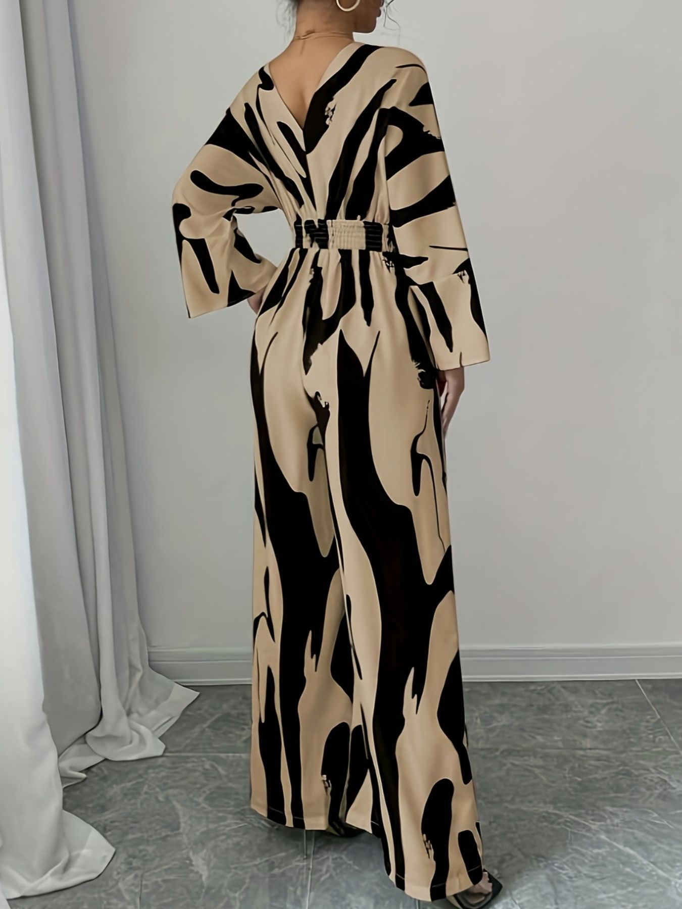 Abstract print wide leg jumpsuit with V-neck, belted waist, and flared sleeves.