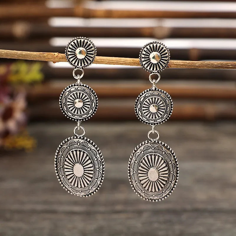 Silver sunburst drop earrings with layered circular and oval pendants.