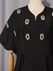 Black midi dress with puff sleeves and rhinestone-embellished green jewels.