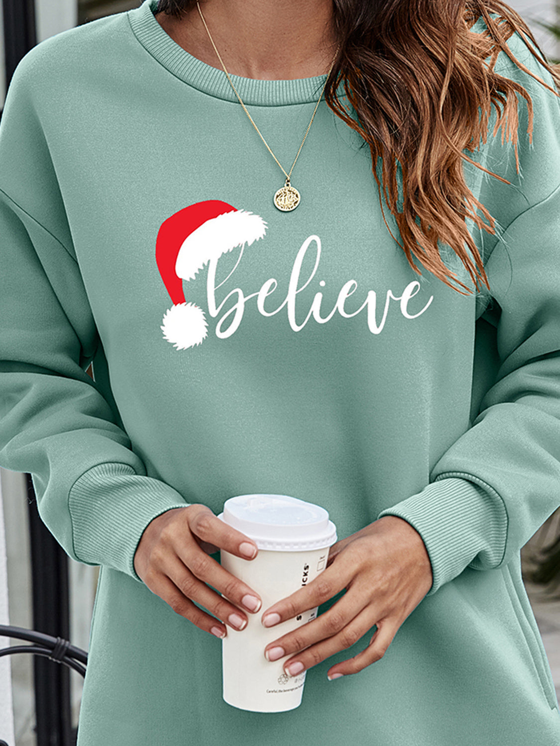 Sage Christmas graphic tunic sweatshirt with Santa hat and "believe" text.