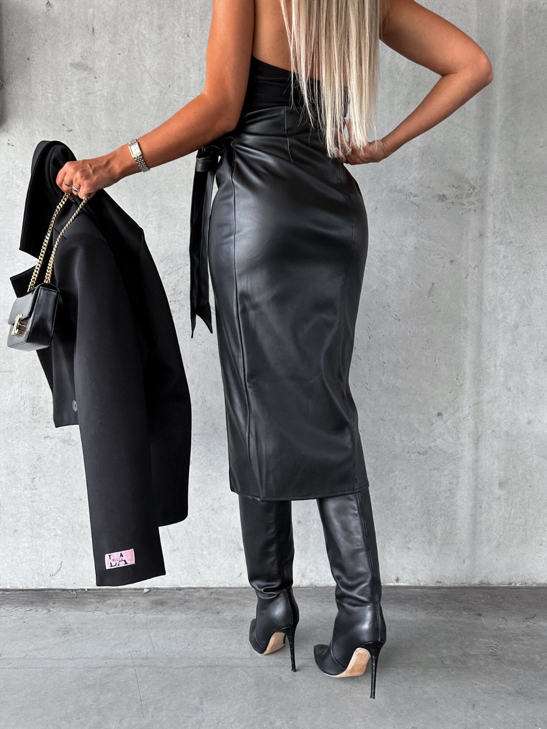 Black faux leather wrap midi skirt with asymmetric hem and tie waist.