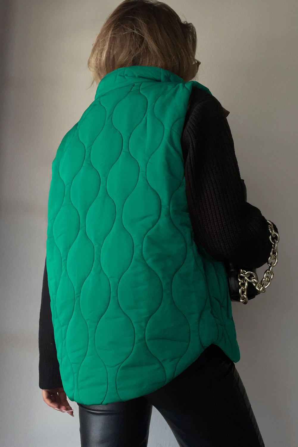 Green quilted stand-collar gilet with wave pattern, worn over a black sweater.
