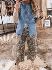 Denim vest with button front and slit detail, worn over a long sleeve top and patterned pants.