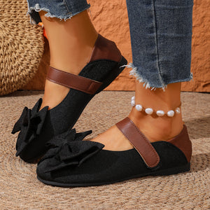 Black round toe flats with bow detail and brown strap, textured fabric.