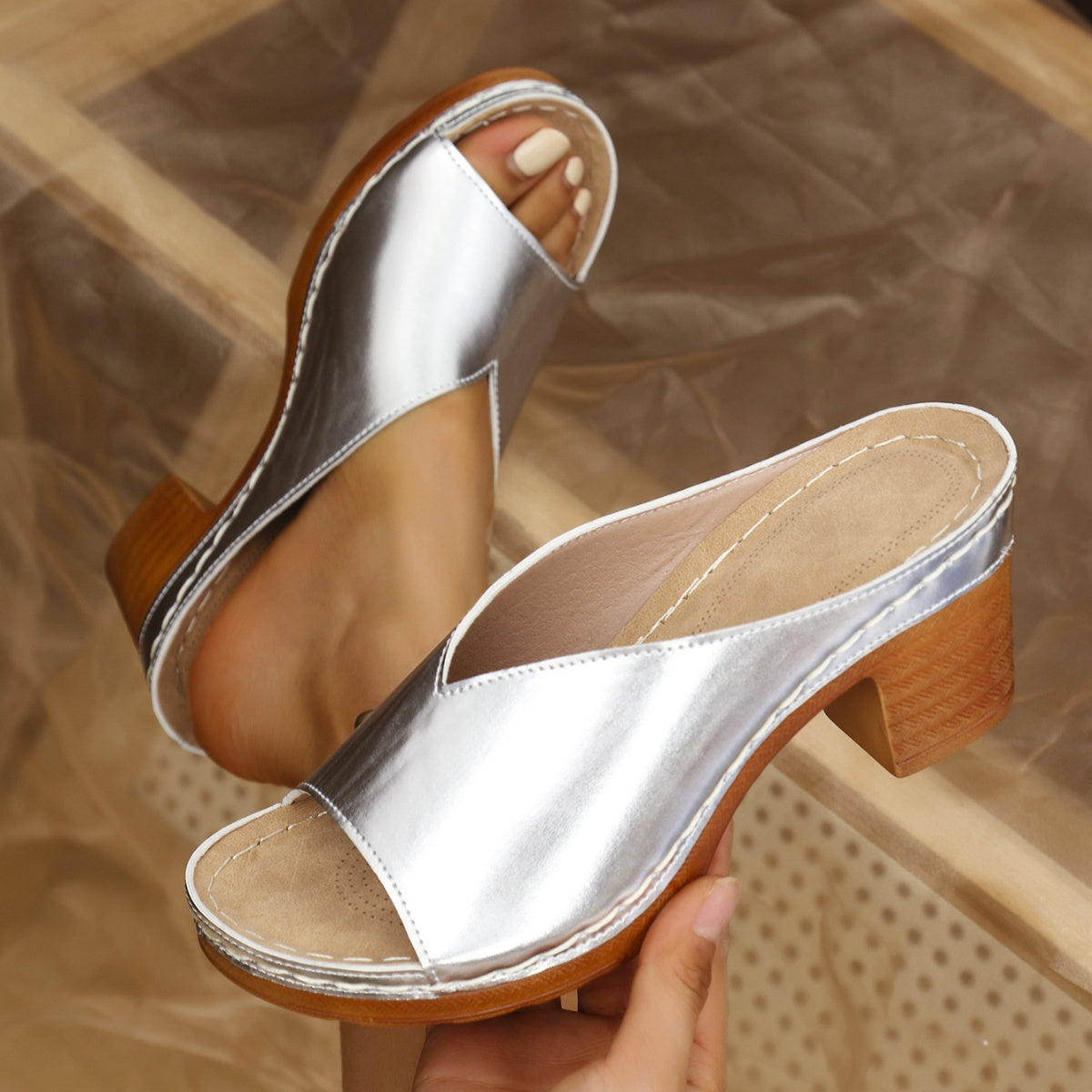 Silver open-toe block heel sandals with a wooden heel detail.